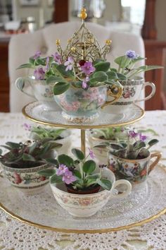 three tiered tray with flowers and tea cups on it, sitting on a table