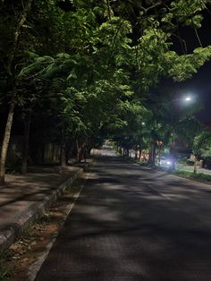 an empty street at night with trees lining the sides and one car parked on the side