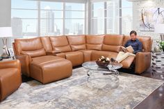 a man sitting on a couch reading a book in a living room with large windows