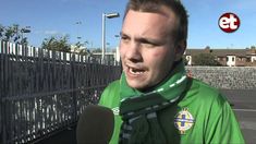 a man in a green shirt is talking to the camera and wearing a scarf around his neck