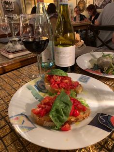 a white plate topped with bread and tomatoes next to a bottle of wine on a table