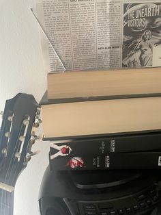 a guitar and some books on top of each other in front of a white wall