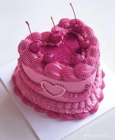 a heart shaped cake with pink frosting and cherries on top, sitting on a white surface