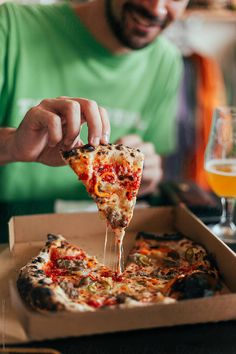 a man is taking a slice of pizza from a box with beer in the background