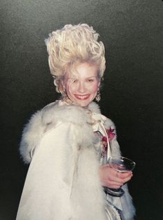 a woman in a white fur coat holding a wine glass and smiling at the camera