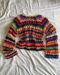 a multicolored knitted sweater laying on top of a white bed coverlet