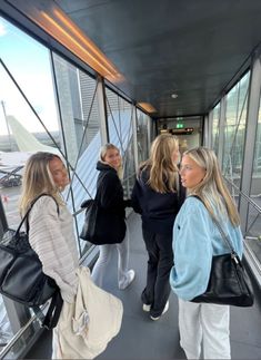 three women are standing on the glass walkway looking at something in the distance while one woman is holding onto her handbag