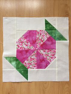 a pink and green patchwork quilt on top of a wooden floor