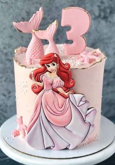 a pink and white cake with a princess figure on it's top, next to the number three