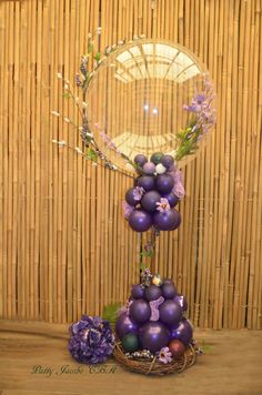 an arrangement of purple eggs and flowers in a basket on a bamboo table with wicker wall