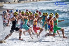 a group of men running in the water at the beach with helmets on their heads