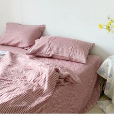 a bed with red and white striped sheets on top of it next to a flower vase