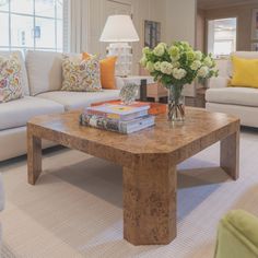 a living room filled with furniture and flowers on top of a coffee table in front of a window