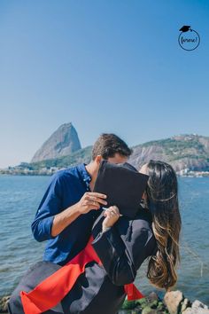 a man and woman are kissing by the water with mountains in the backgroud