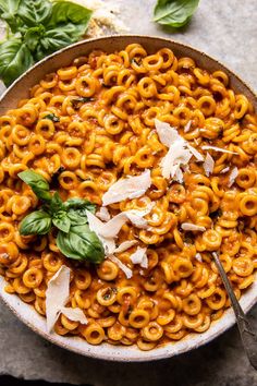 a bowl filled with pasta and sauce on top of a table next to basil leaves