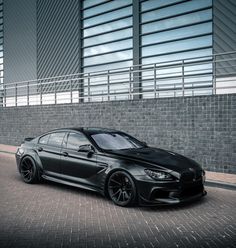 a black car parked in front of a brick wall next to a tall building with windows