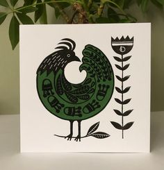 a red and black rooster on a white card next to a potted green plant