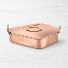 a large copper serving dish with handles on a white marble countertop, in the shape of a hexagonal box