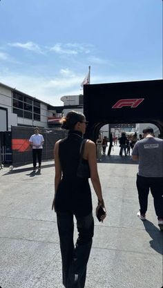 a woman walking down the street in front of a race track with other people standing around