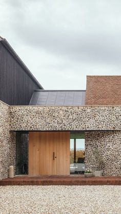 a modern house with stone walls and wooden doors on the front door is surrounded by gravel