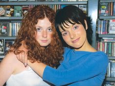 two women standing next to each other in front of bookshelves