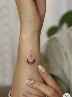 a woman's hand with a small tattoo on her left wrist and the moon behind her arm