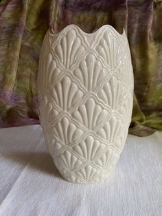 a white vase sitting on top of a table next to a green and purple curtain