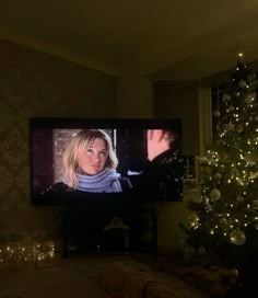 a woman is watching tv in front of the christmas tree