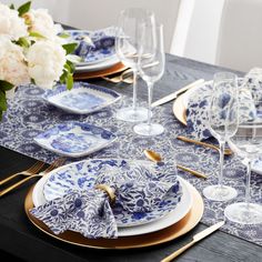 a table set with blue and white plates, silverware and gold place settings on it