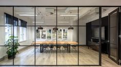 an office with glass walls and wooden tables in the foreground is seen through large windows