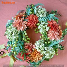 a wreath with flowers and scissors on a pink tableclothed surface, ready to be made into an ornament