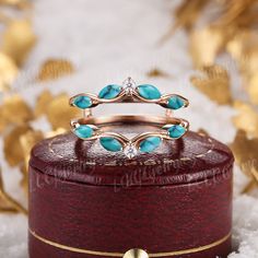 two rings with turquoise stones are sitting on top of a red box in the snow