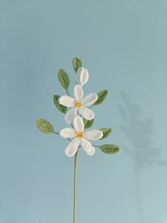 a crocheted white flower with green leaves on a blue background is shown in the foreground