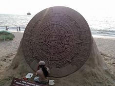 a person sitting in front of a sand sculpture on the beach