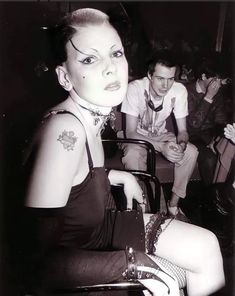 a black and white photo of a woman with tattoos on her neck sitting in a chair