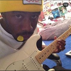 a man wearing a yellow beanie and holding a white guitar in front of his face