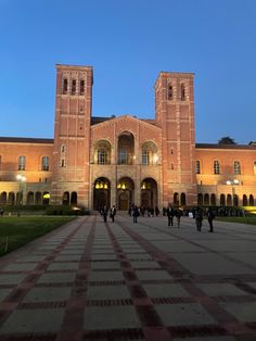 people walking in front of a large building with two towers at the end of it