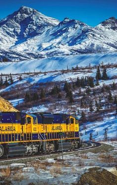 a yellow and blue train traveling past snow covered mountains