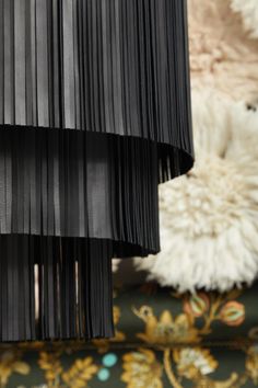 black pleated lampshade hanging on wall next to white fur rug and chair