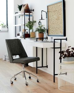 a chair sitting in front of a white desk with plants on it and a framed art piece