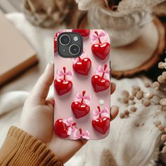 a person holding up a cell phone case with hearts and bows on it in front of some flowers