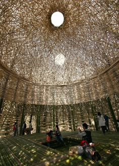 people are sitting on the ground under a bamboo structure that looks like it is made out of sticks