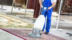 a man in blue overalls cleaning a rug with a machine