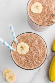 two glasses filled with smoothie and bananas on a white table next to each other