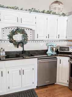 a kitchen with white cabinets and black counter tops, silver appliances and a wreath on the wall