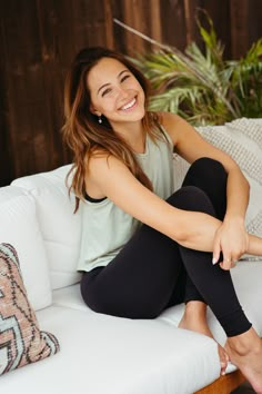 a woman sitting on a white couch smiling at the camera while wearing black leggings