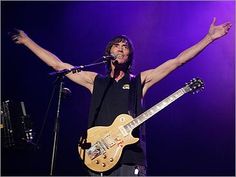 a man holding his arms up in the air while singing into a microphone and guitar