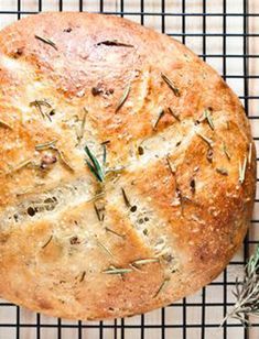 a loaf of bread sitting on top of a cooling rack next to a sprig of rosemary