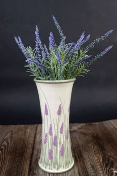 a white vase filled with purple flowers on top of a wooden table