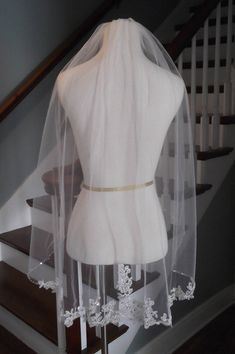 the back of a wedding dress with a veil on display in front of some stairs